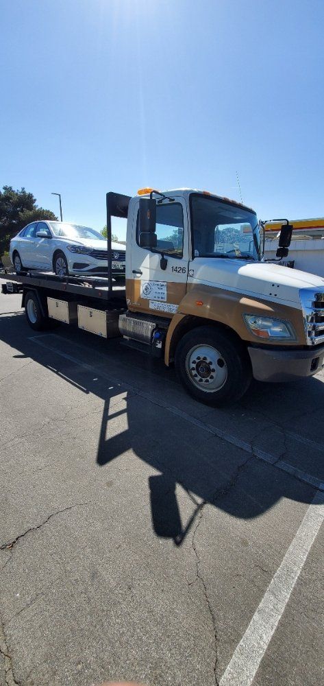 A white sedan loaded on a tow truck, parked on asphalt under a sunny sky.