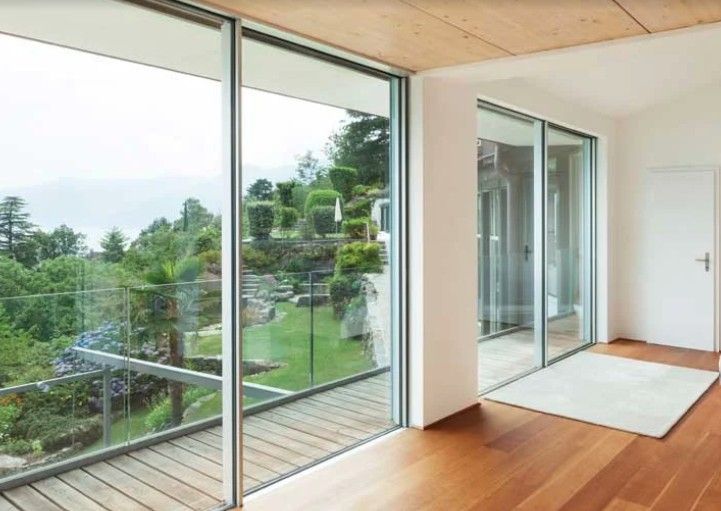 Interni luminosi con pavimenti in legno, grandi porte scorrevoli in vetro che si aprono su un rigoglioso giardino e un tappeto bianco.