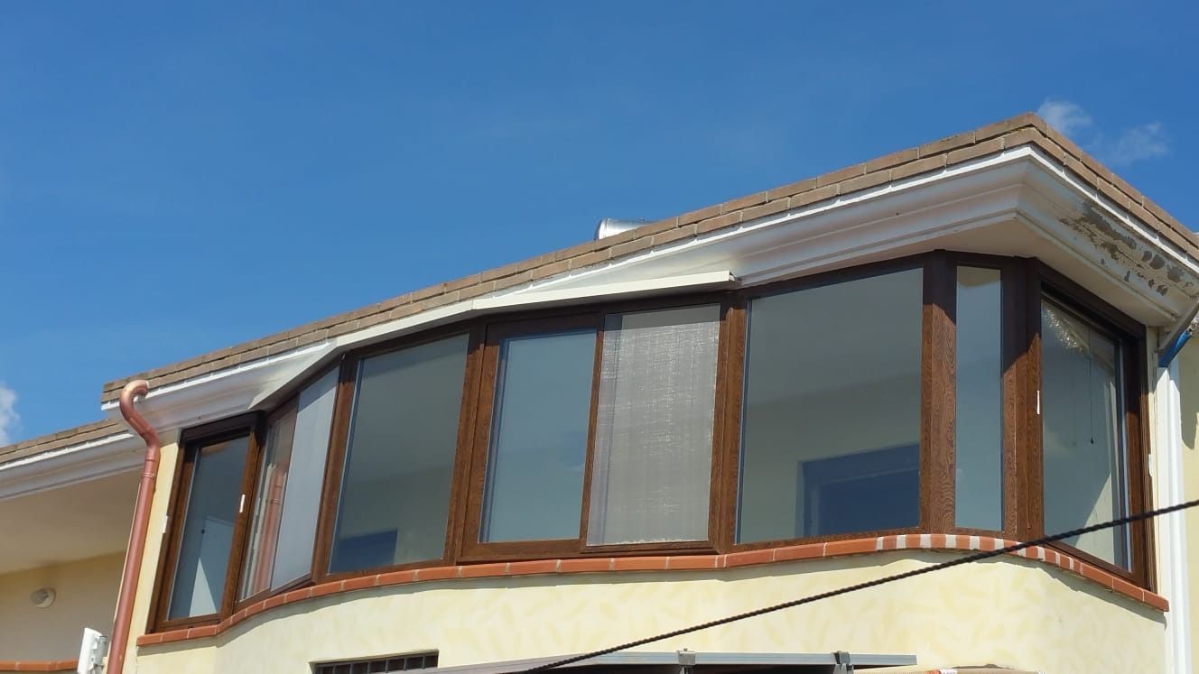 Finestra a bovindo con cornici marroni su un edificio sotto un cielo azzurro.