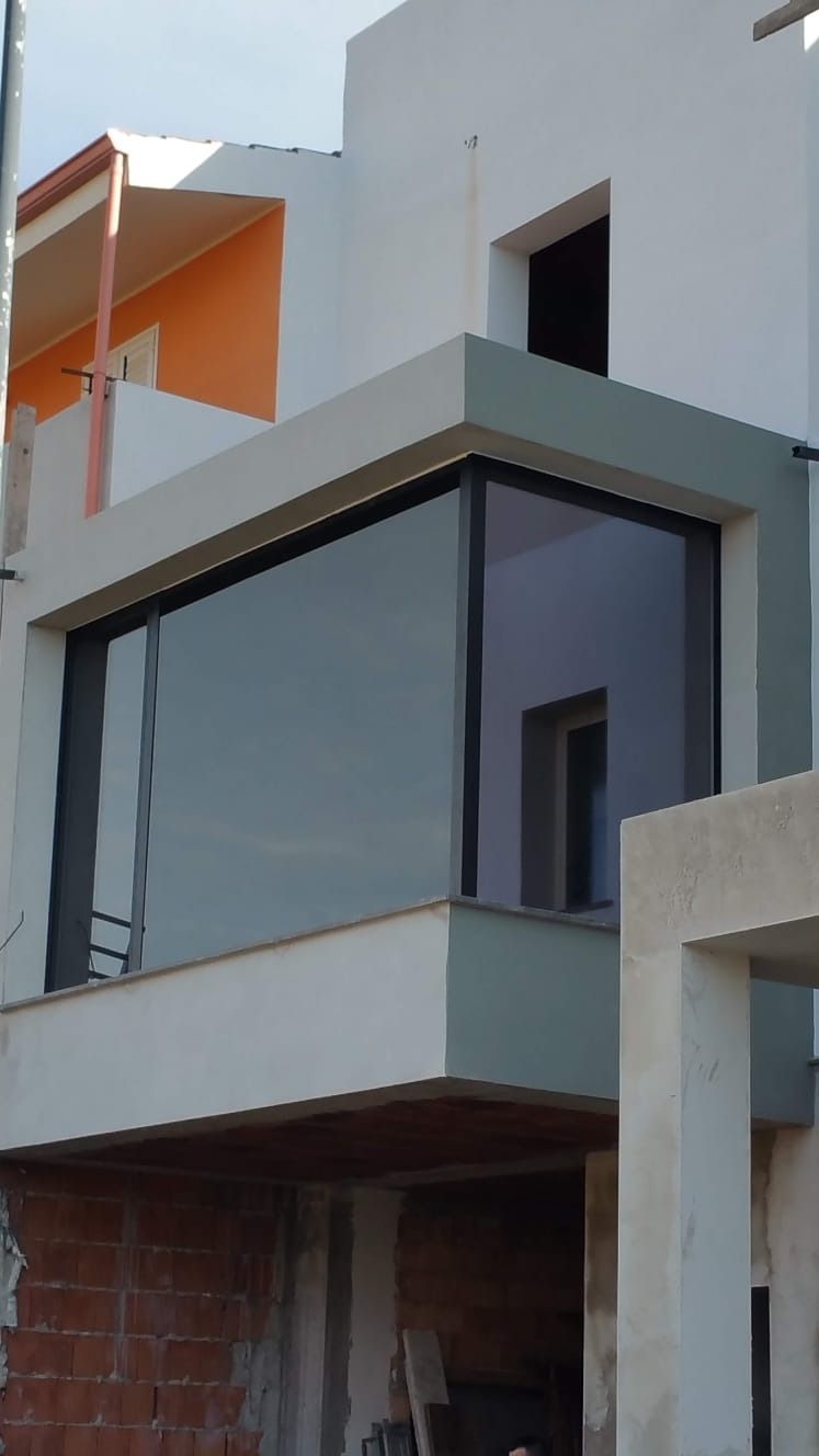 Edificio moderno con grandi vetrate e pareti di colore chiaro; balcone arancione visibile.