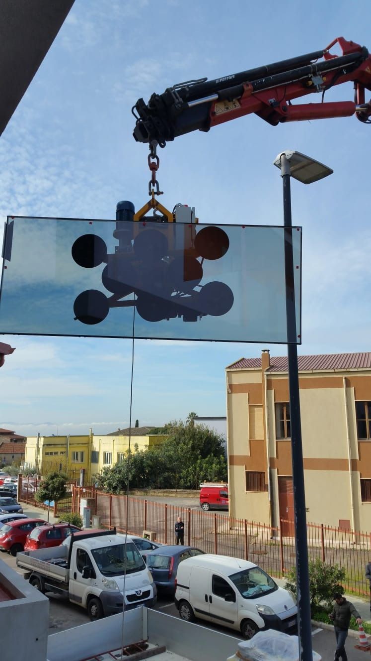 Gru che solleva una grande lastra di vetro su una strada cittadina. Ventose per fissare il vetro. Giornata di sole, contesto residenziale.