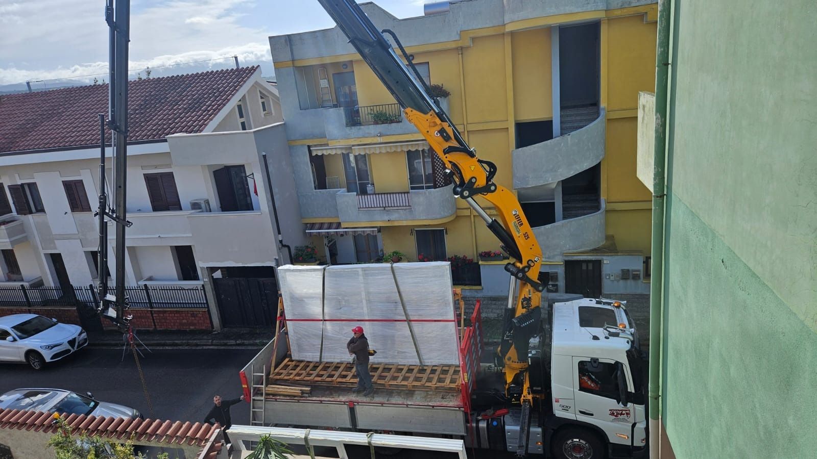 Gru che scarica materiali vicino agli edifici. Un operaio è in piedi sul cassone del camion.