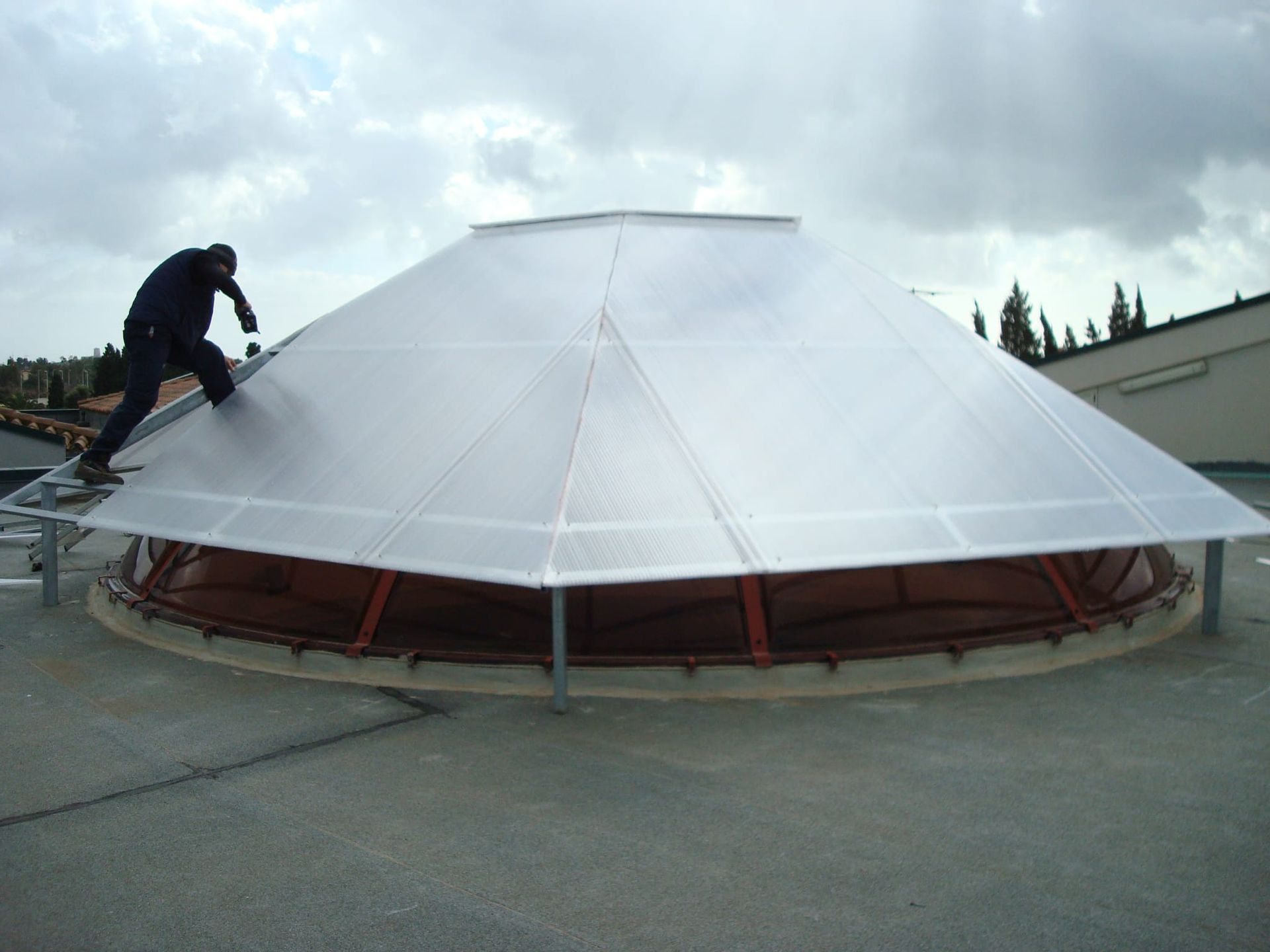Persona sul tetto che installa un grande lucernario trasparente e geometrico su un edificio.