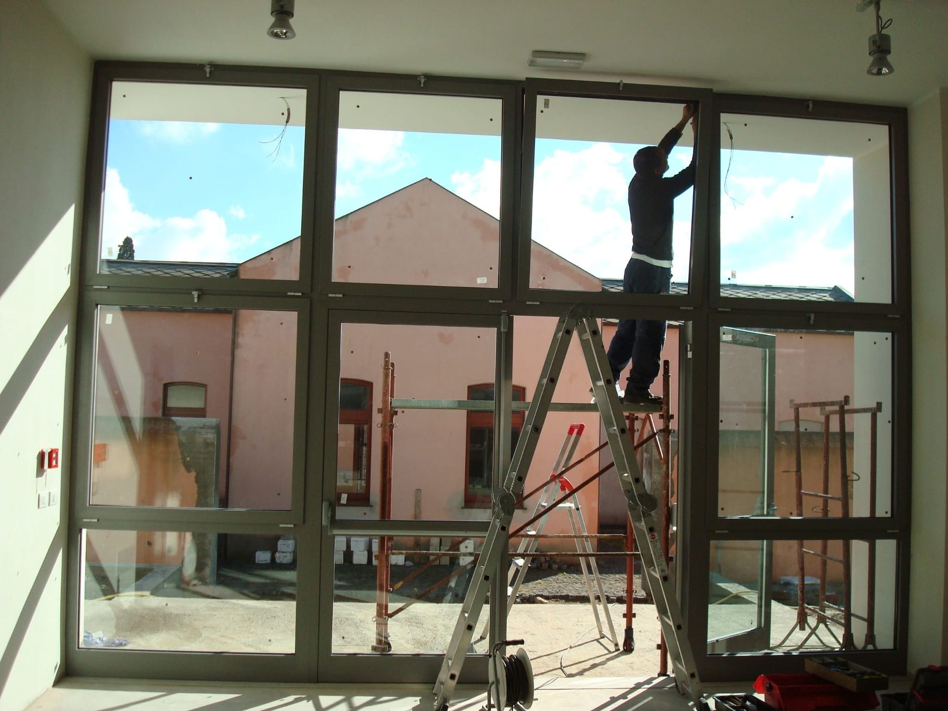 Persona su una scala che installa qualcosa su un grande telaio di finestra. Un edificio rosa visibile attraverso la finestra.