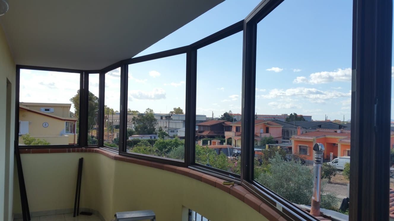 Vista interna di un balcone con vetrate che si affacciano sulla città e sul cielo azzurro.