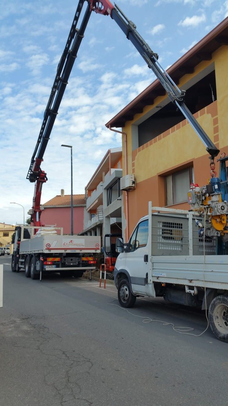 Attrezzatura di sollevamento per autogru, cassone di un camion pieno di materiali, ambientazione stradale, un edificio sullo sfondo.