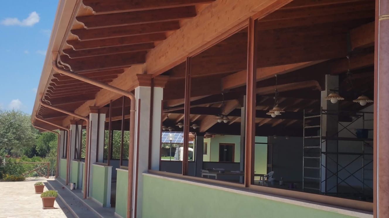 Edificio con struttura in legno e ampie finestre. Tetto e pilastri marroni su una parete verde. Luminoso durante il giorno.