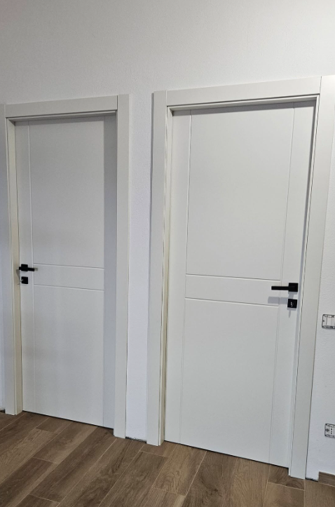 Due porte interne bianche con maniglie nere e scanalature orizzontali, inserite in cornici bianche, contro una parete bianca.