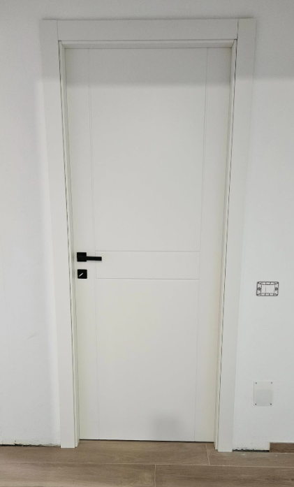 Porta bianca con maniglia e finiture nere su una parete bianca.