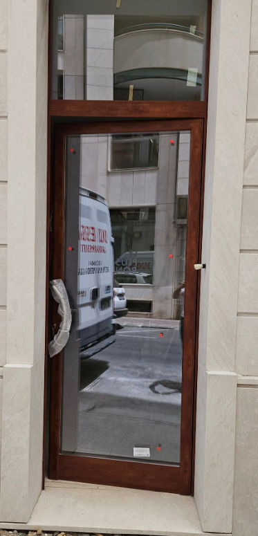 Porta a vetri socchiusa con cornice in legno scuro e maniglia, da cui si può ammirare la strada esterna.