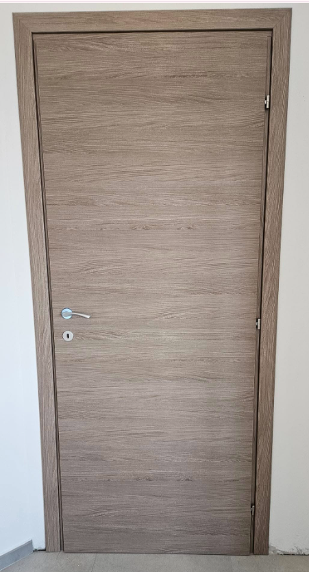 Una porta interna chiusa con finitura effetto legno marrone chiaro, ferramenta argentata e telaio di colore chiaro.