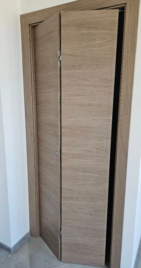 Porta pieghevole in legno, parzialmente aperta, con telaio in legno chiaro.