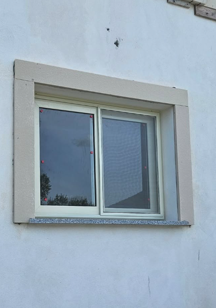 Finestra su muro bianco con finiture in pietra beige.