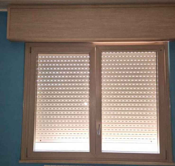 Finestra a due vetri con persiane chiare chiuse e cornice in legno, contro una parete blu.