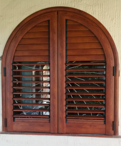 Persiane ad arco in legno con stecche aperte, su una parete di colore chiaro.