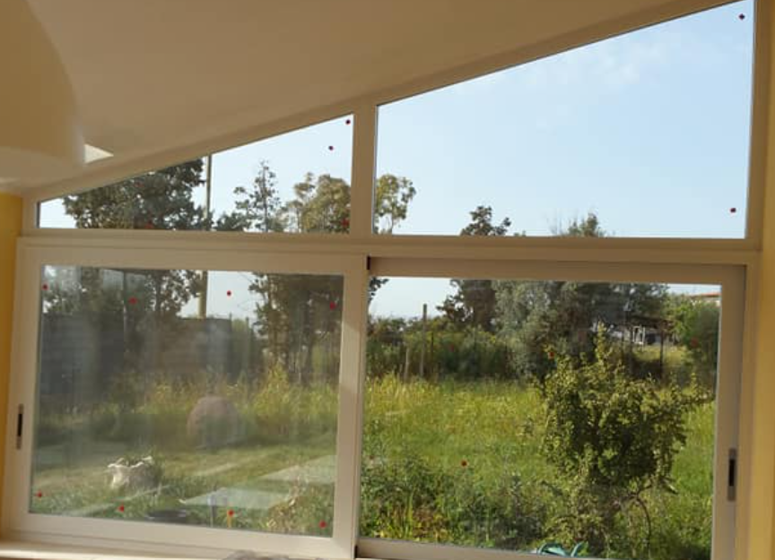 Finestre con cornice bianca con vista su un cortile erboso e alberi, sotto un cielo azzurro.