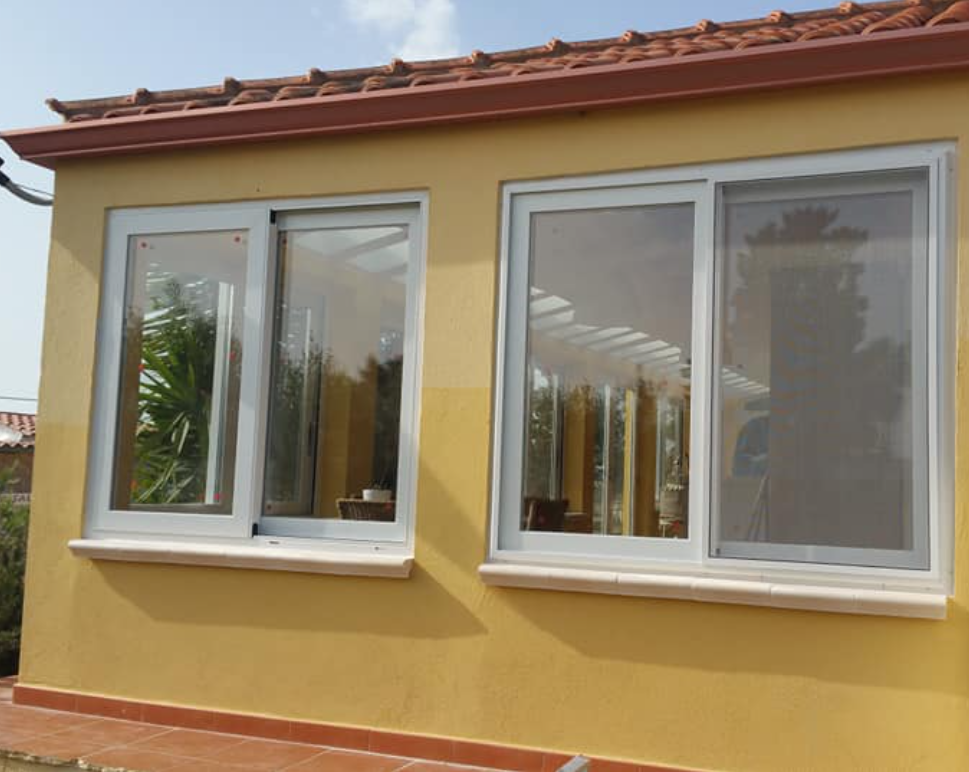 Edificio giallo con finestre scorrevoli bianche; tetto con tegole rosse e davanzali in pietra.