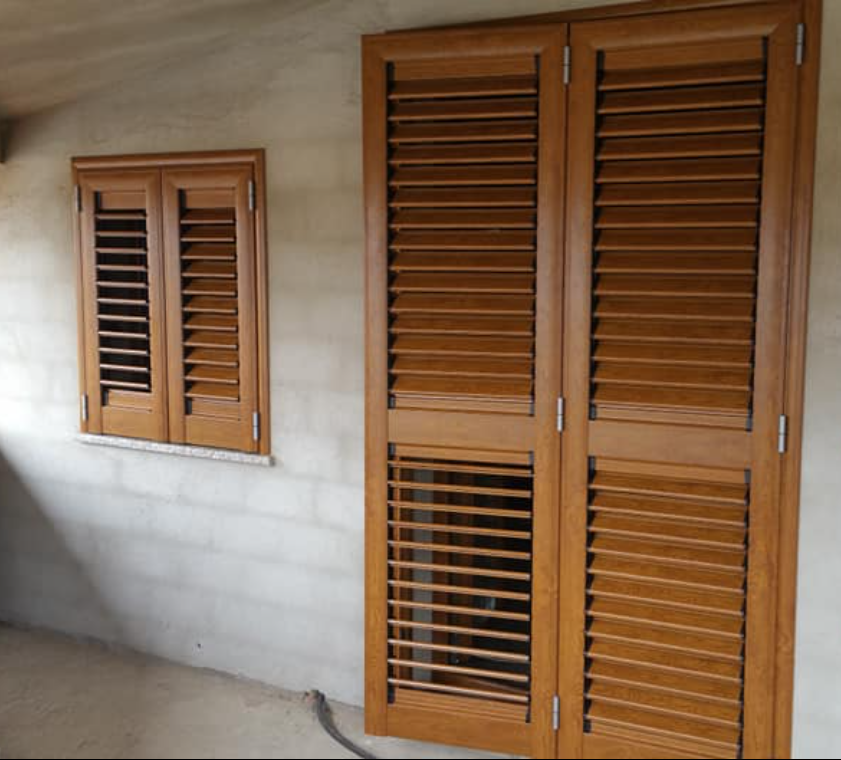 Persiane in legno su una finestra e porte a due battenti, tutte tinteggiate in marrone medio.