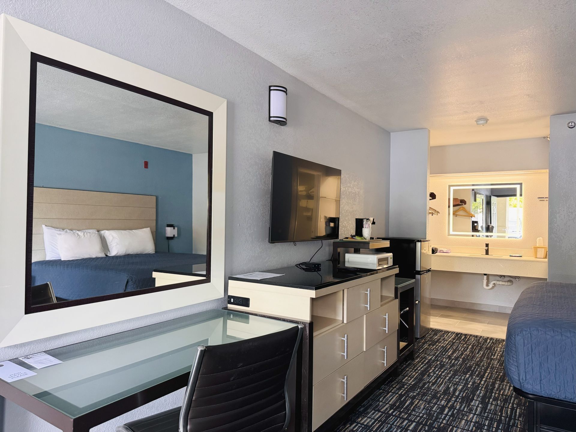 A hotel room with a bed , desk , chair , television and mirror.