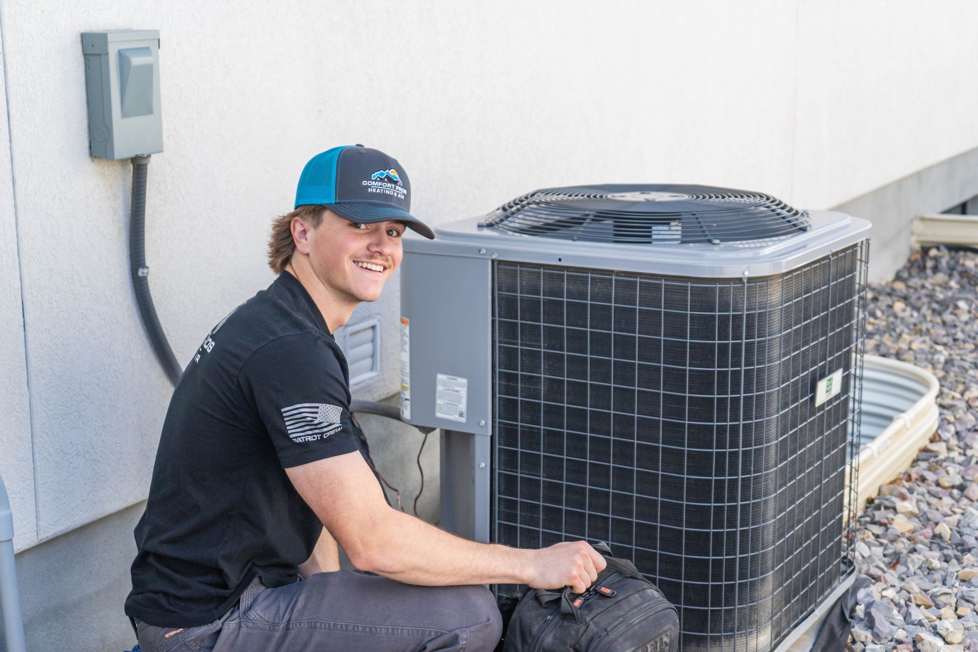 Two air conditioners are sitting on gravel outside of a house.