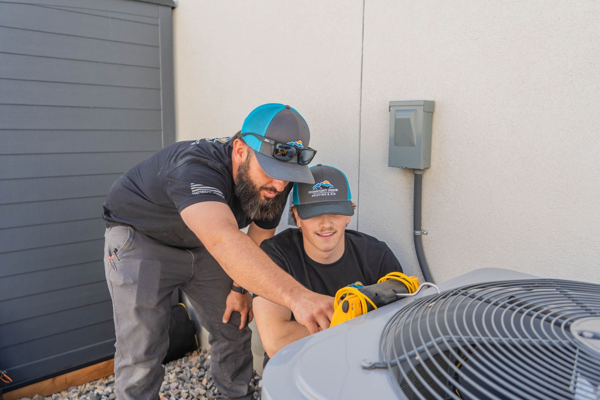 Two men are working on an air conditioner outside of a brick building.