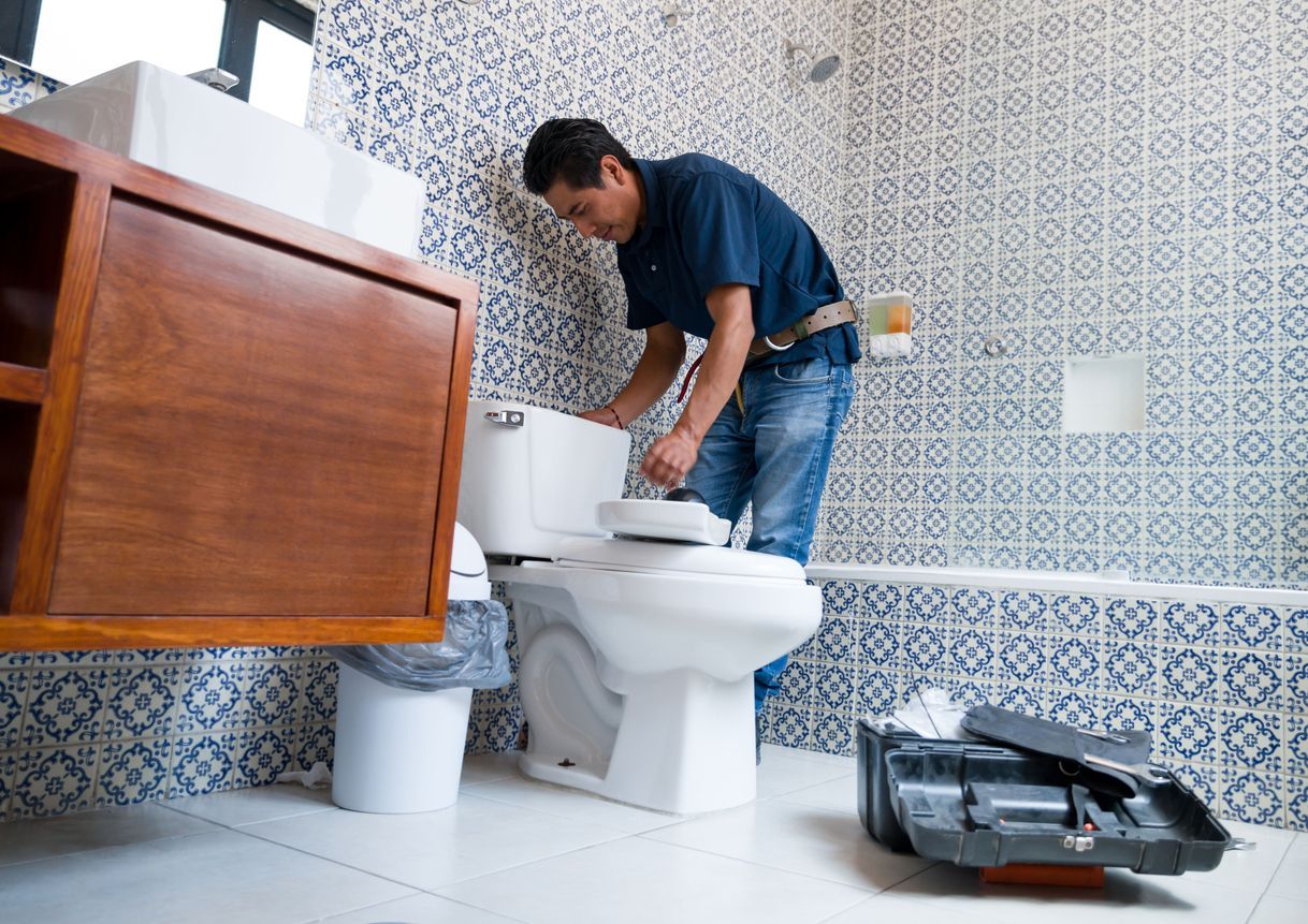 A man is fixing a toilet in a bathroom.