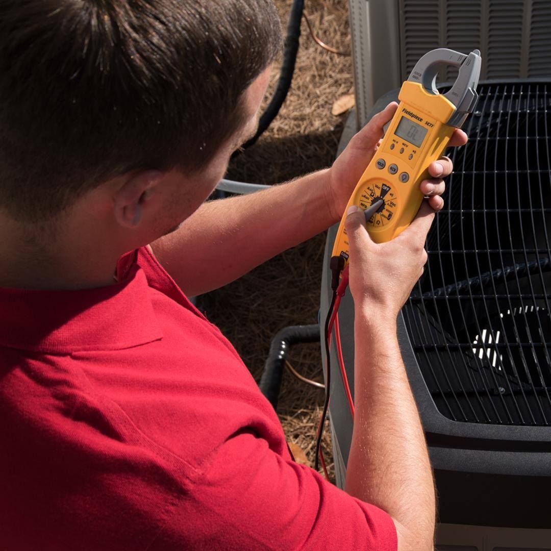 A man in a red shirt is holding a clamp meter