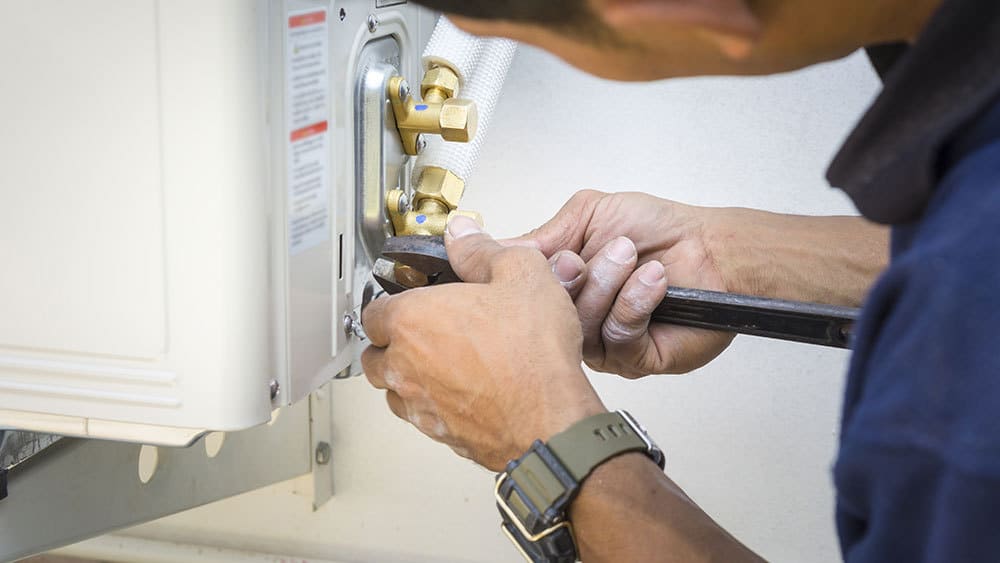 A man is fixing an air conditioner with a wrench.