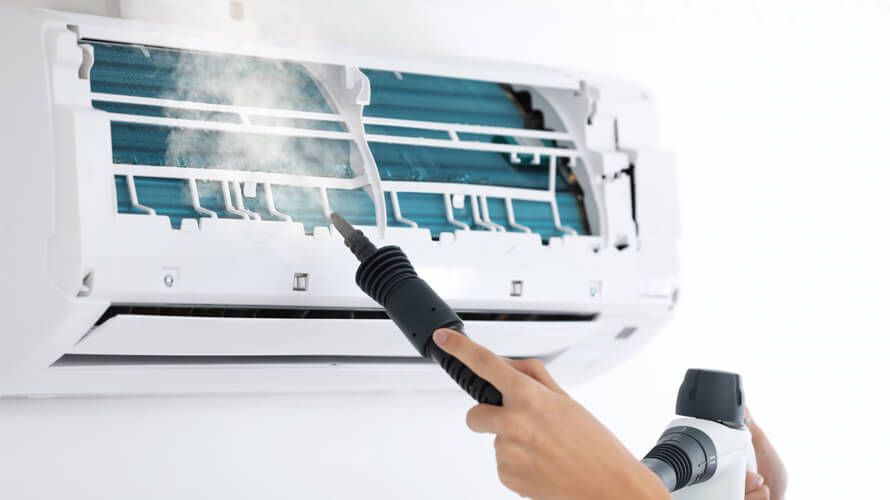 A person is cleaning an air conditioner with a vacuum cleaner.