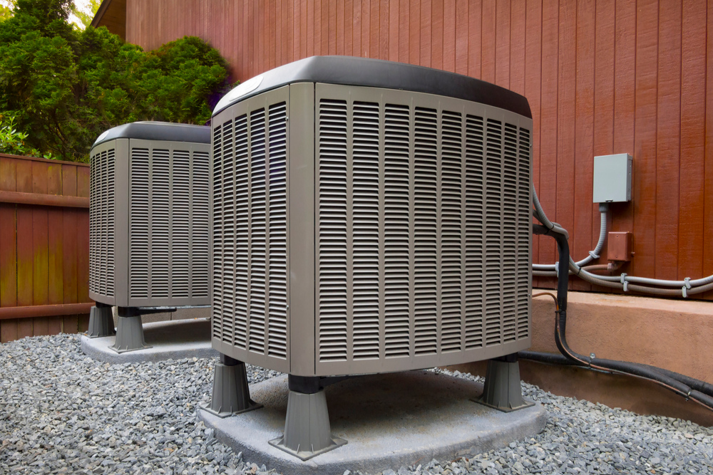 Two air conditioners are sitting next to each other outside of a house.