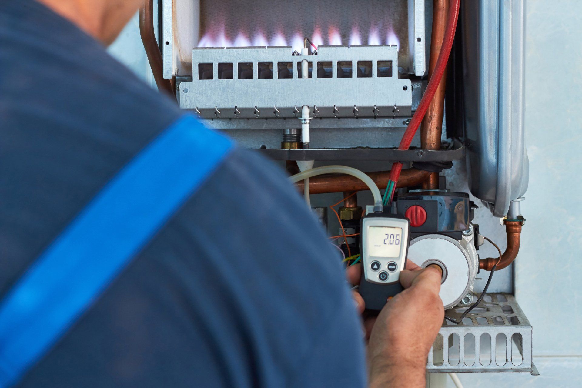 A man is working on a gas boiler with a digital thermometer.