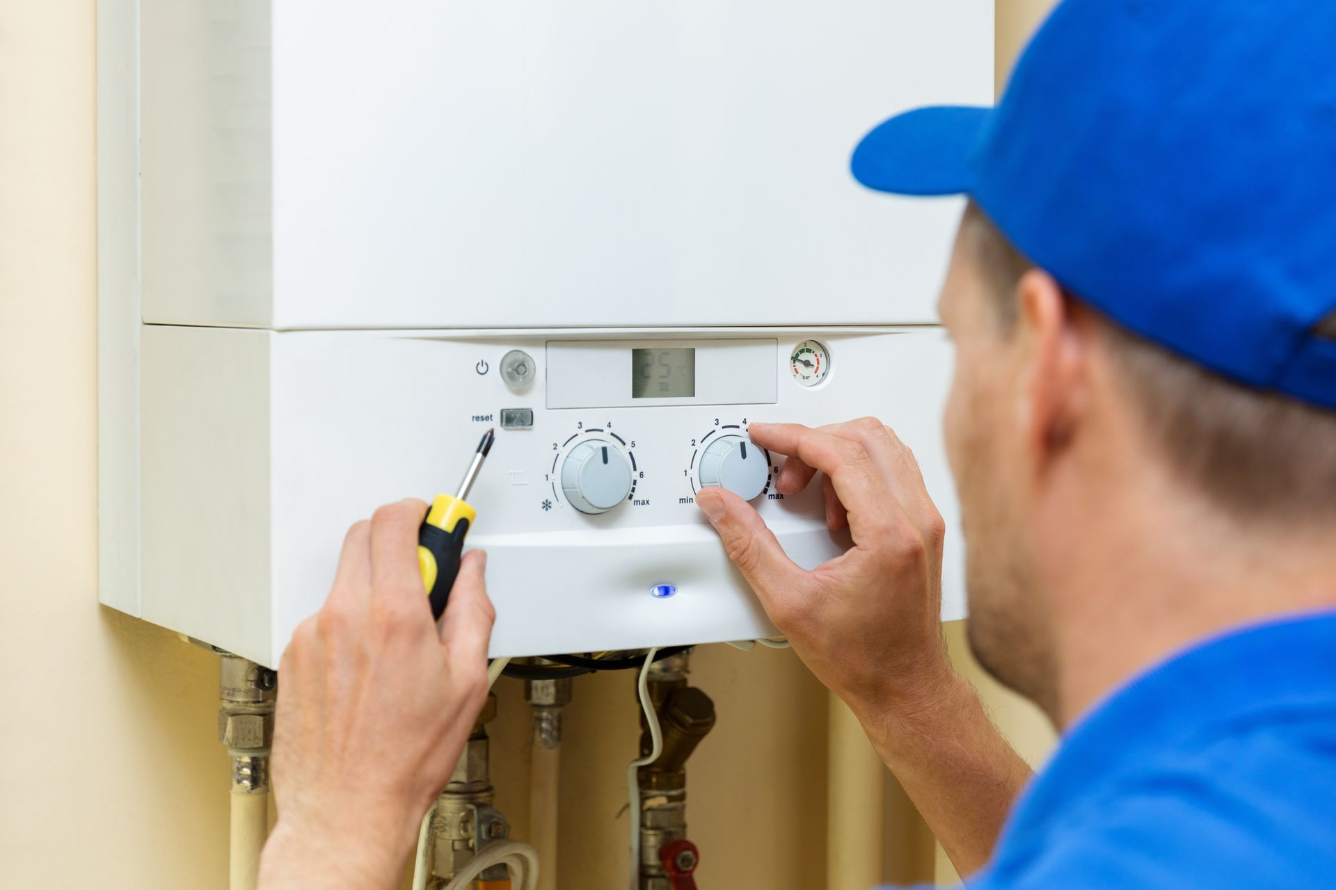 A man is fixing a boiler with a screwdriver.