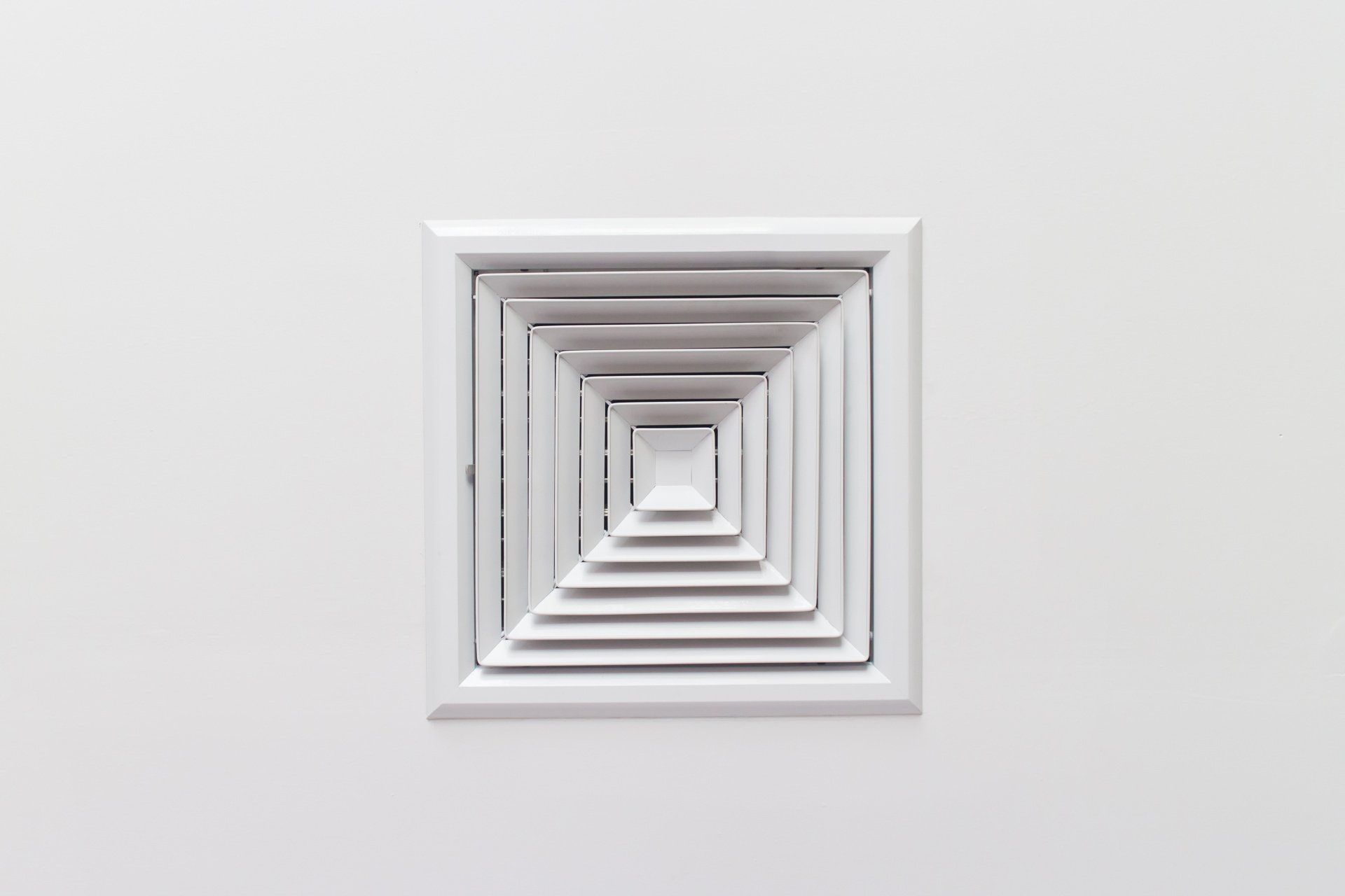 A white square air vent on a white wall.