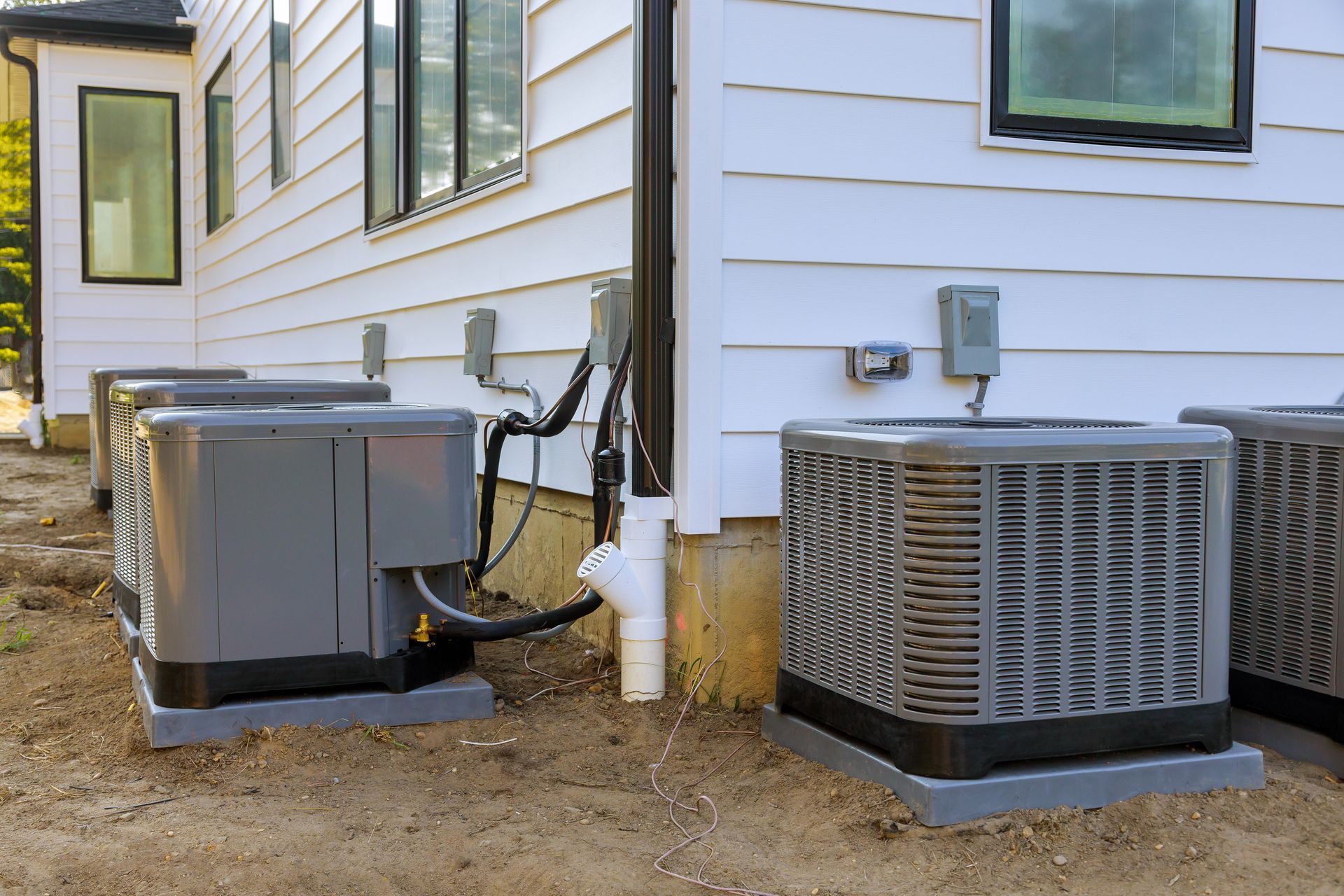 Two air conditioners are sitting next to each other on the side of a house.