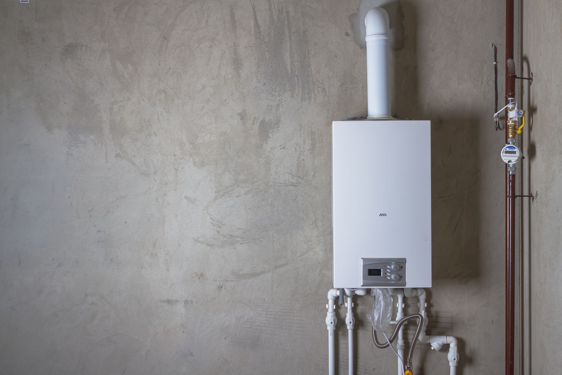 A white boiler is hanging on a wall next to pipes.