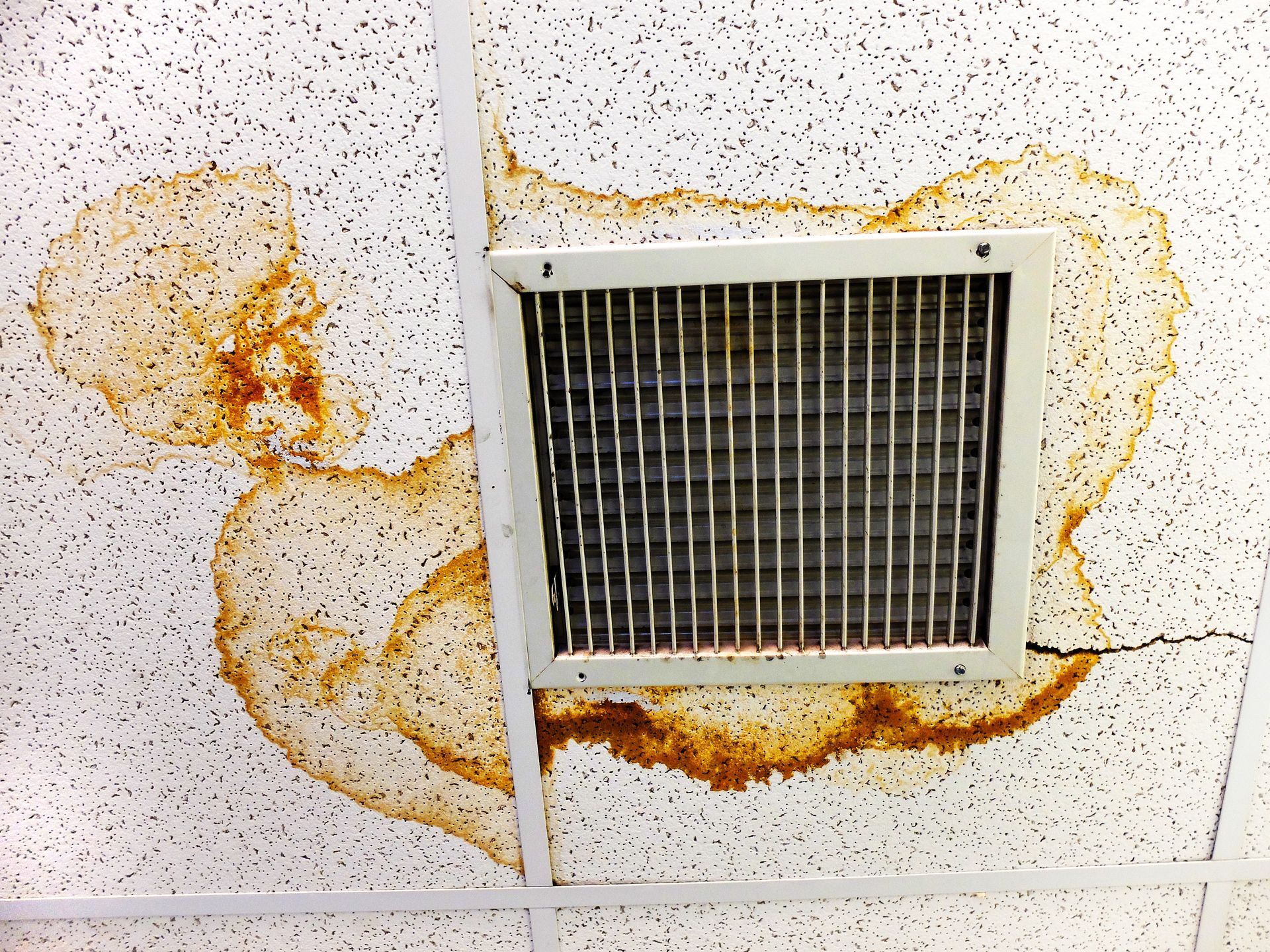 A ceiling with a vent and a stain on it