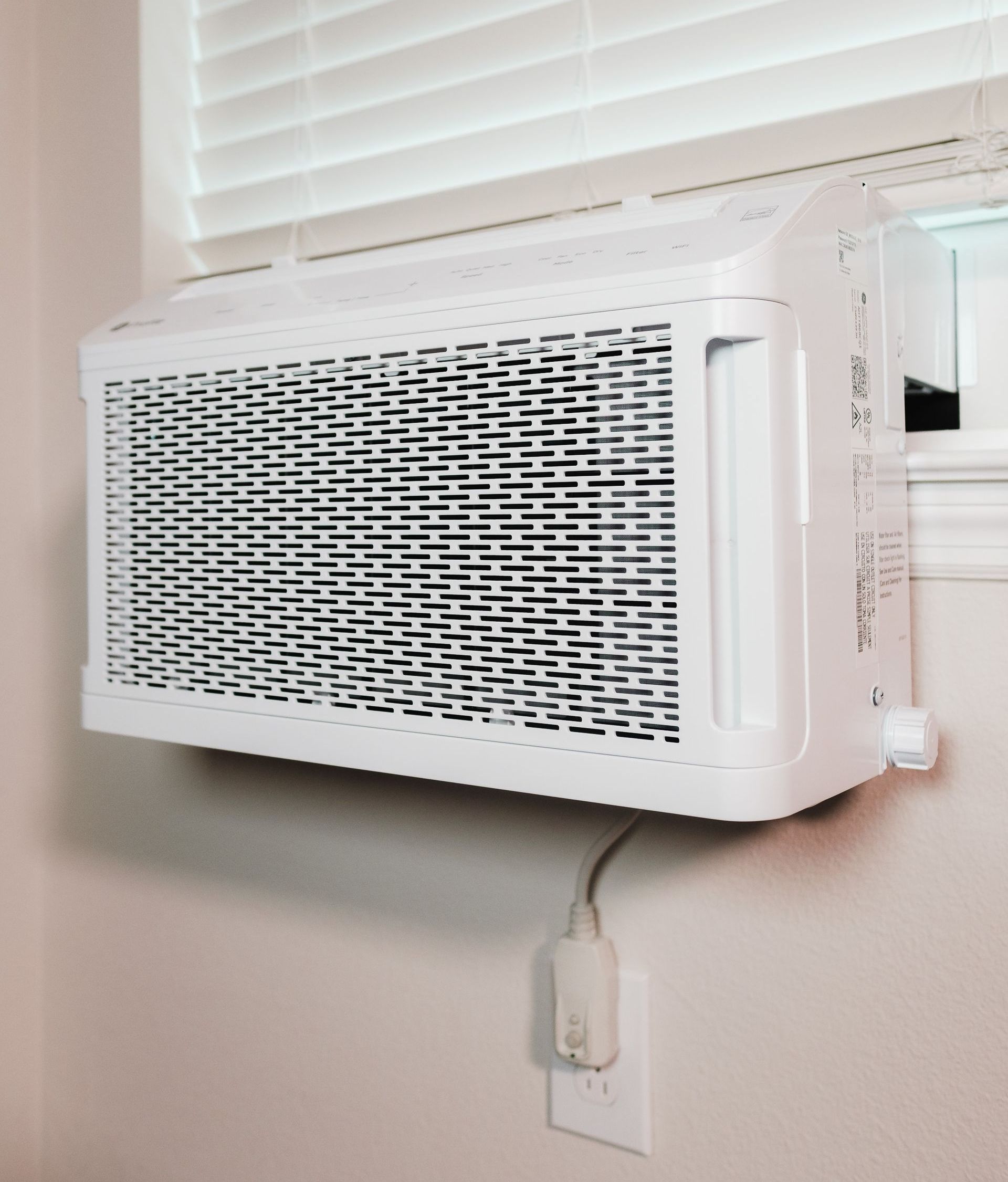 A white air conditioner is mounted to a wall next to a window