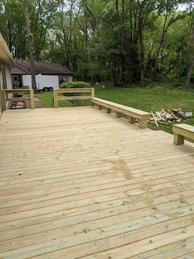 Wooden deck with built-in benches, backyard setting with trees and a house in the background.