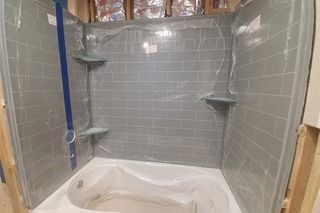 Gray tiled shower stall under construction, with corner shelves and bathtub.