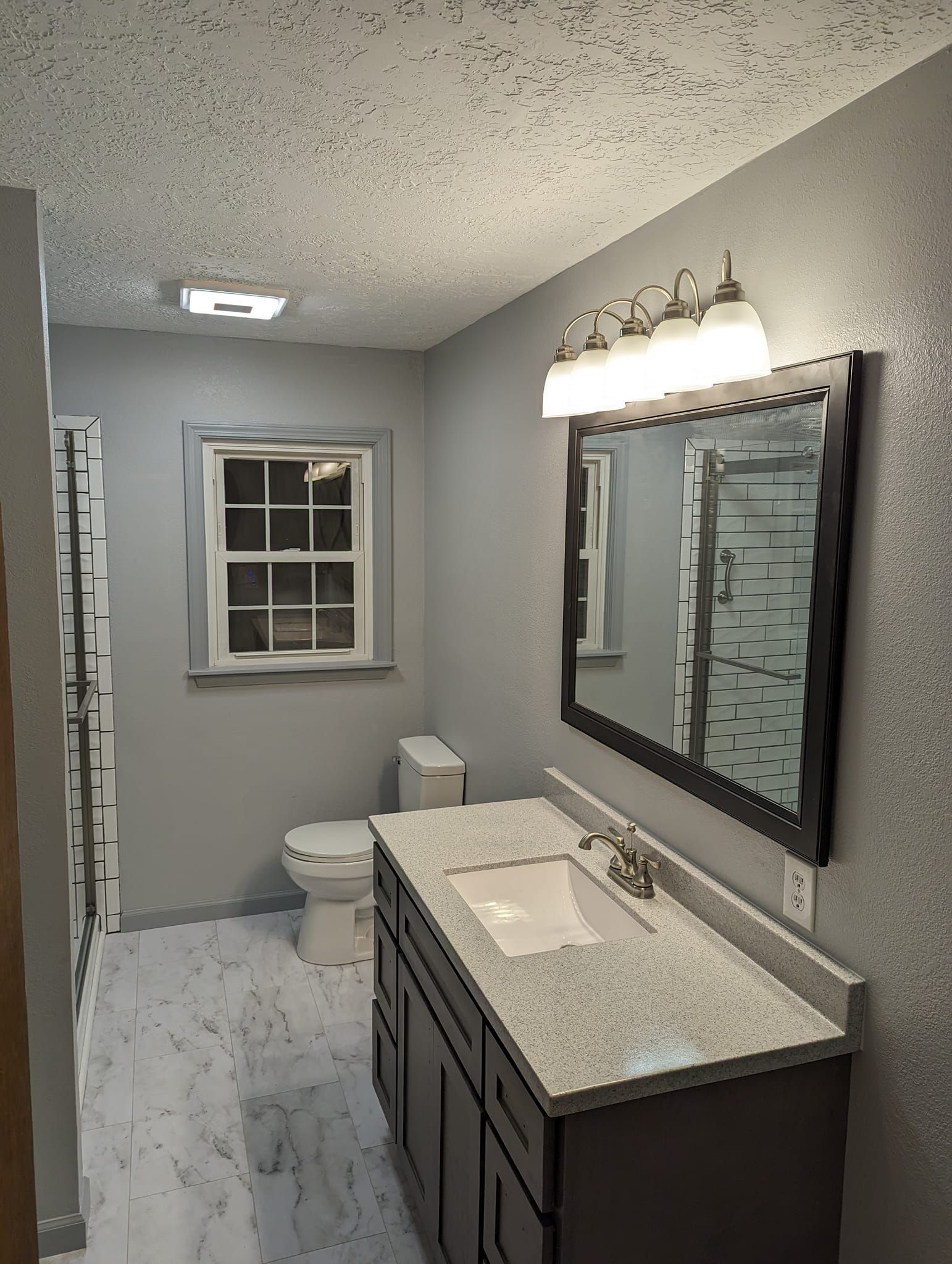 Gray bathroom with vanity, toilet, window, and textured ceiling; white floor.