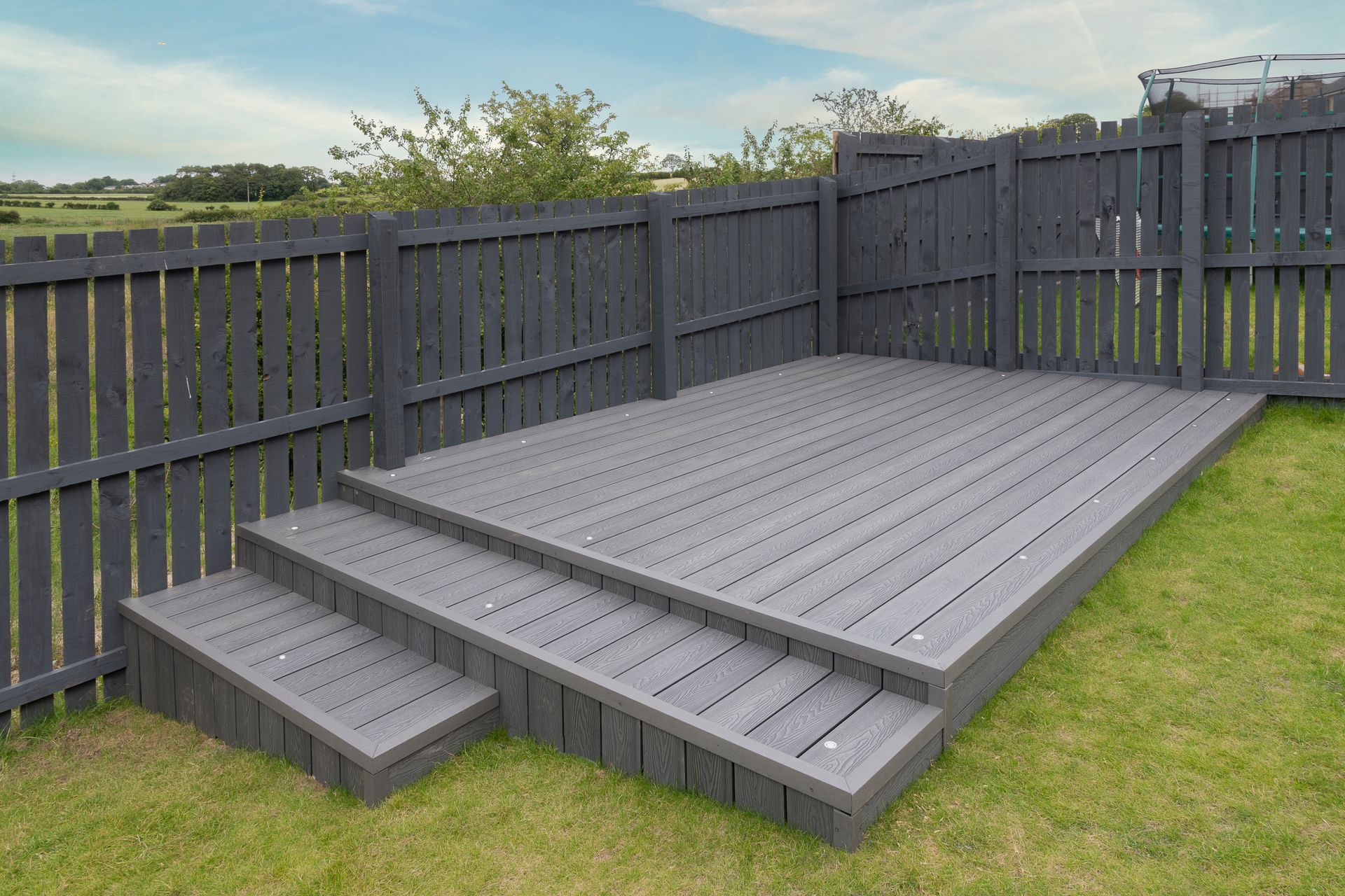 Gray composite deck with steps, surrounded by a gray picket fence, on a green lawn.