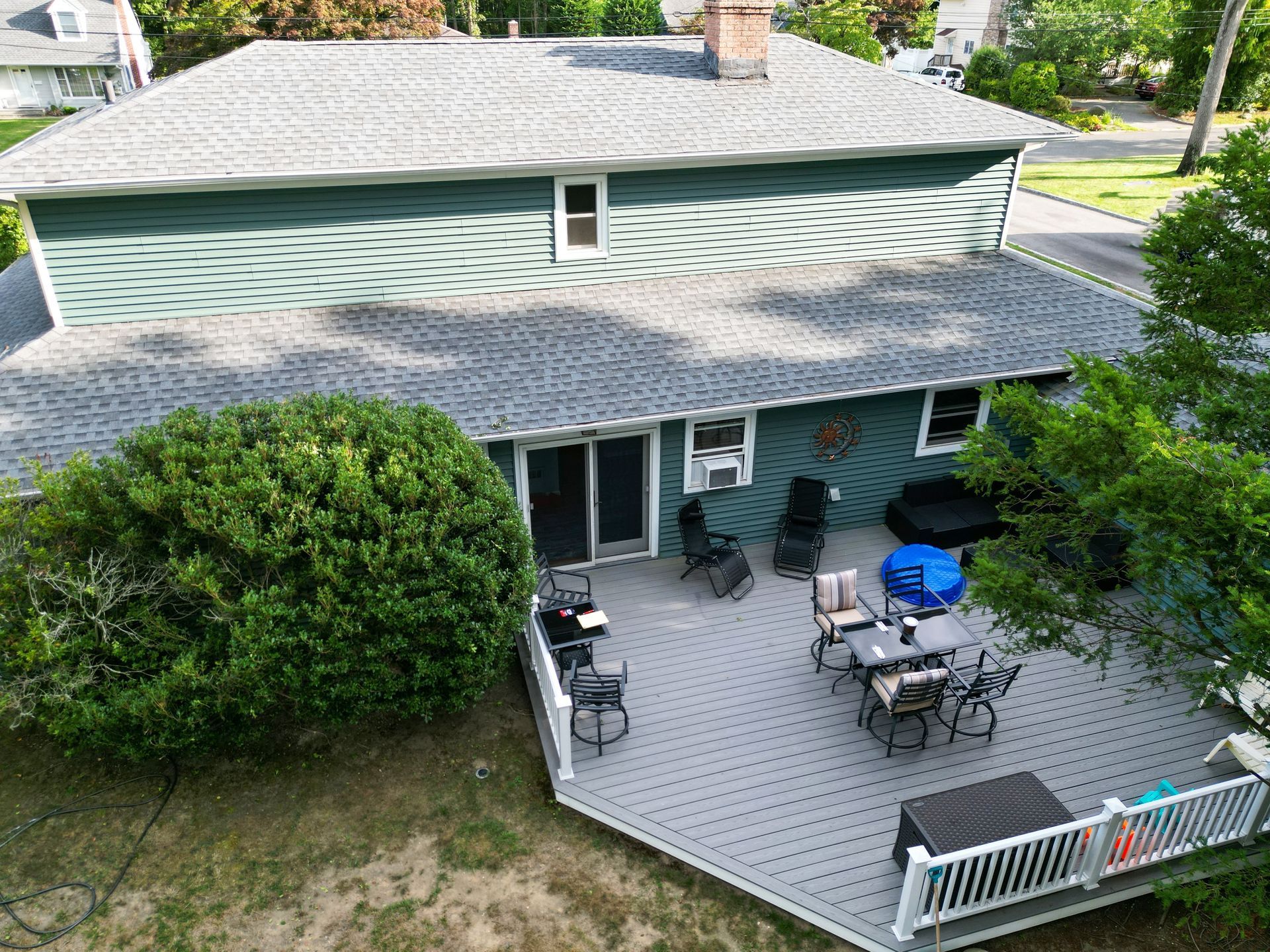 Overhead view of a two-story house with a gray deck, outdoor furniture, and green siding.