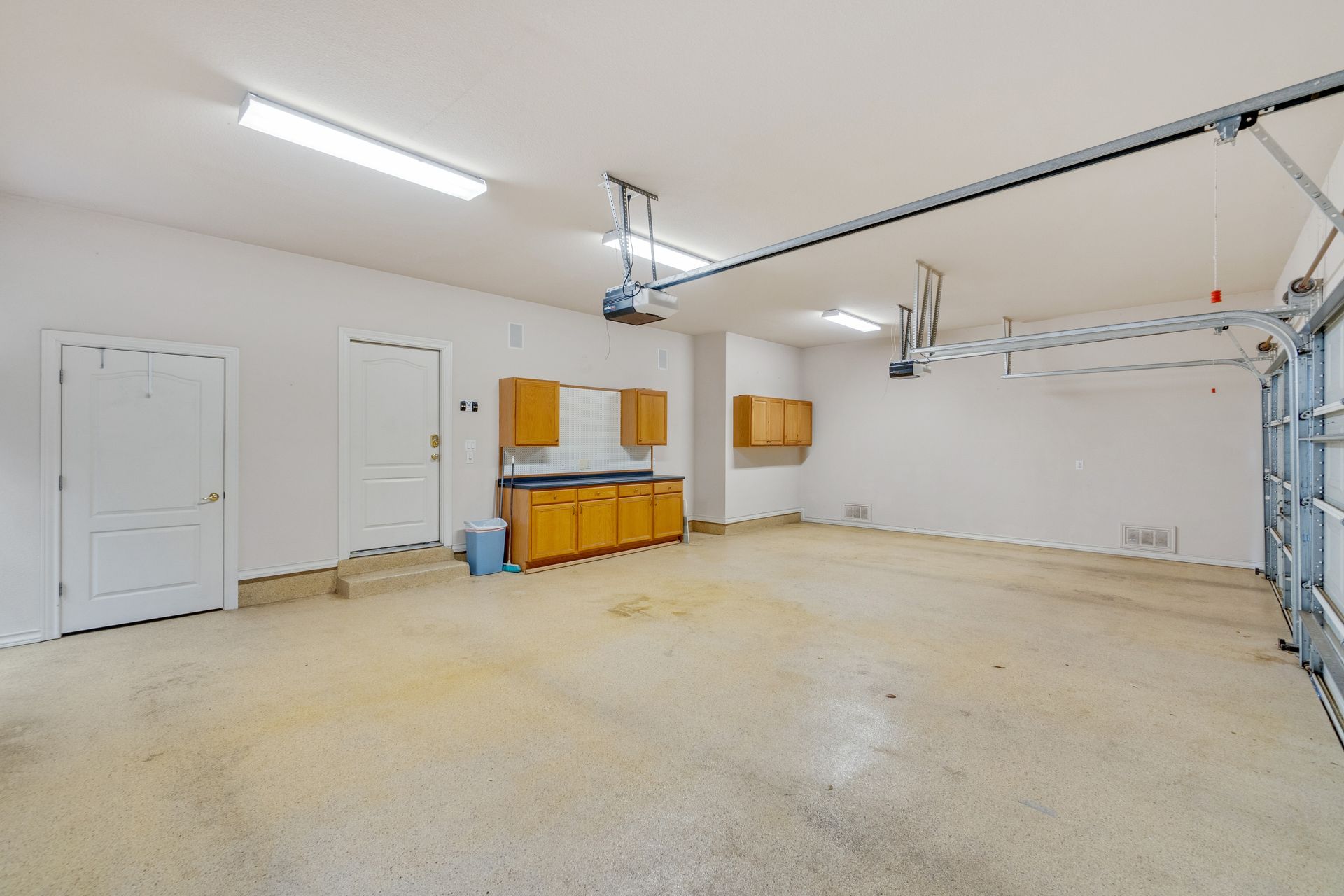 Empty, well-lit garage with a closed garage door, cabinets, and two doors.