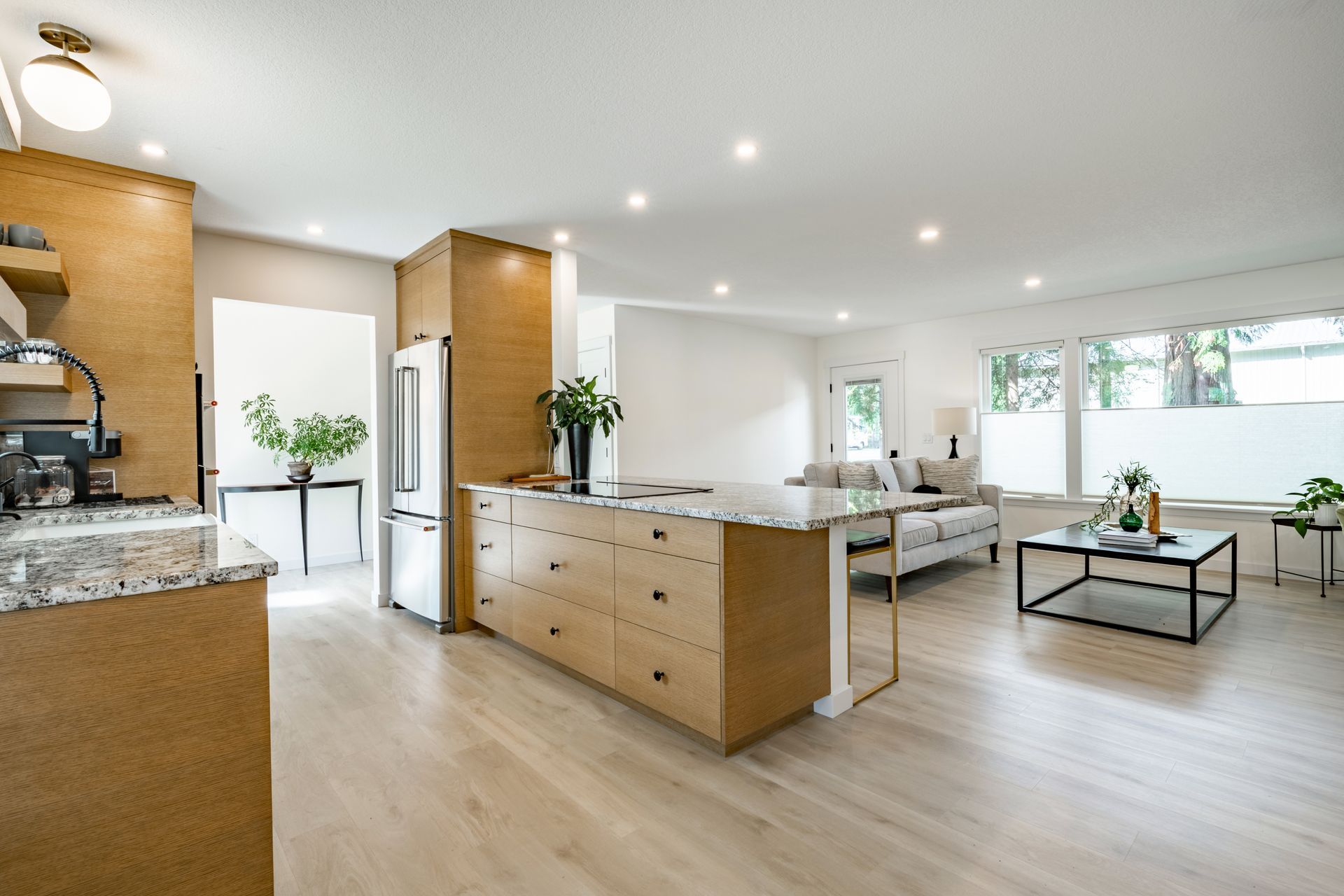 Open-concept kitchen and living room with light wood floors, tan cabinets, and a marble island.