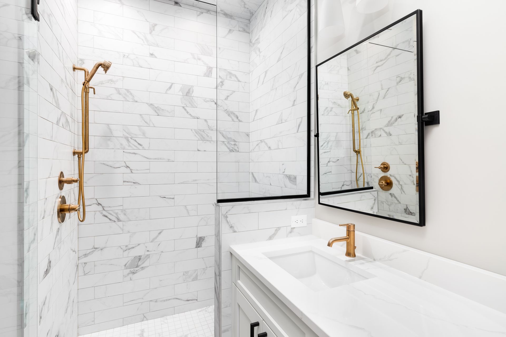 Marble bathroom with gold fixtures: shower, sink, and mirror. White and gray tones.