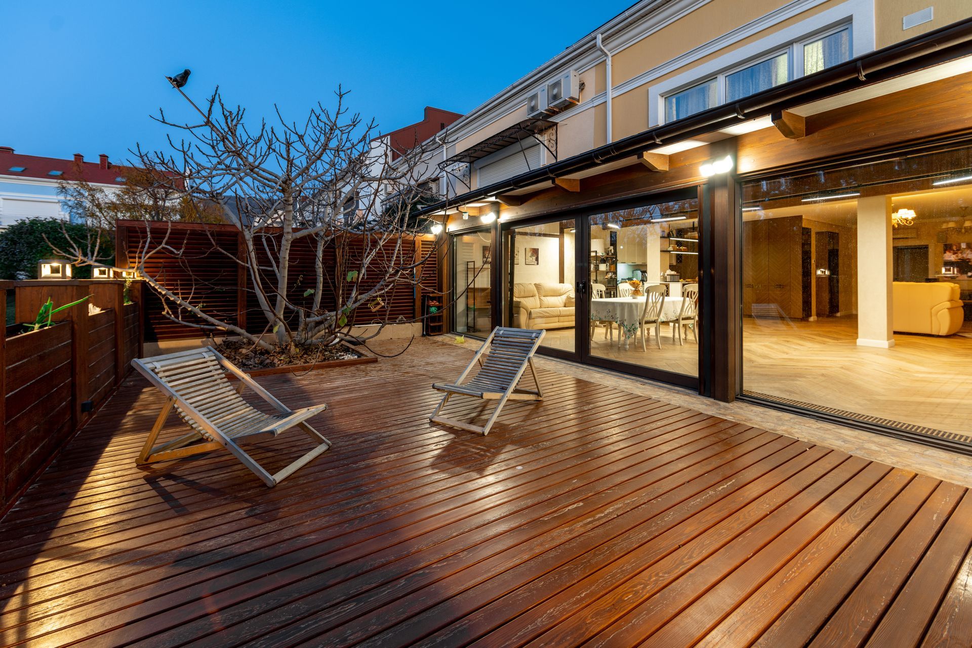 Wooden deck with chairs, leading into a lit interior through sliding glass doors.