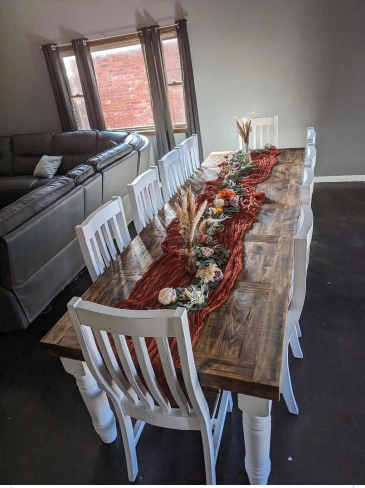 Long rustic dining table set for a fall gathering, with centerpiece of flowers and pumpkins.