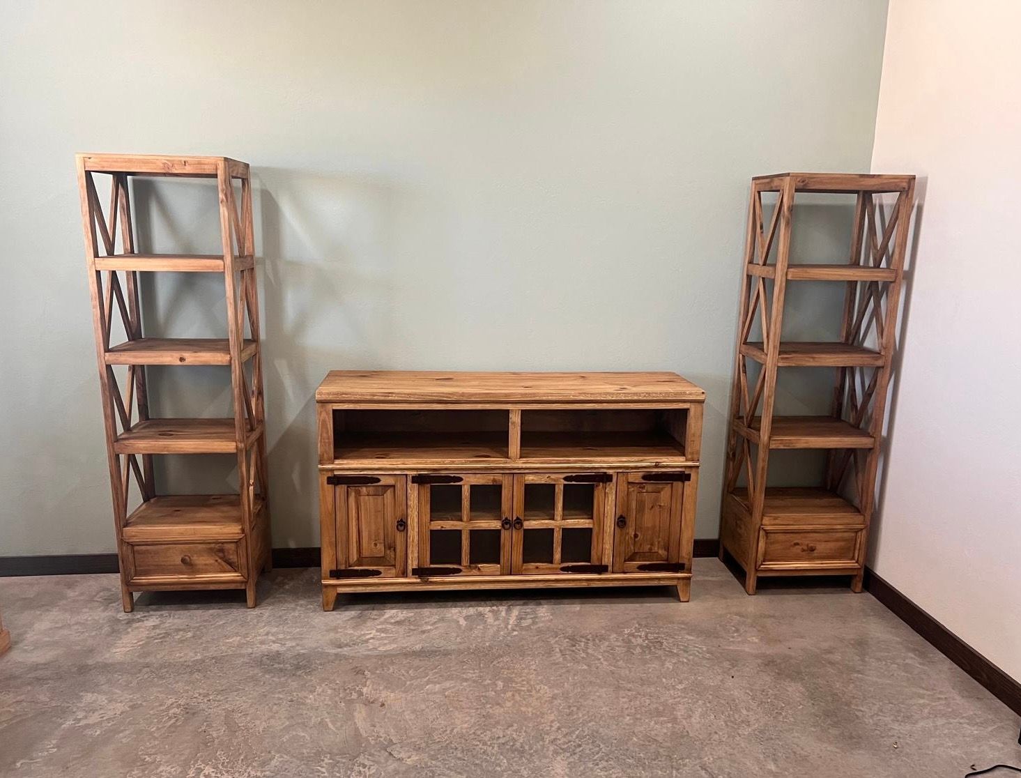 Wooden entertainment center with two side bookshelves against a pale green wall.