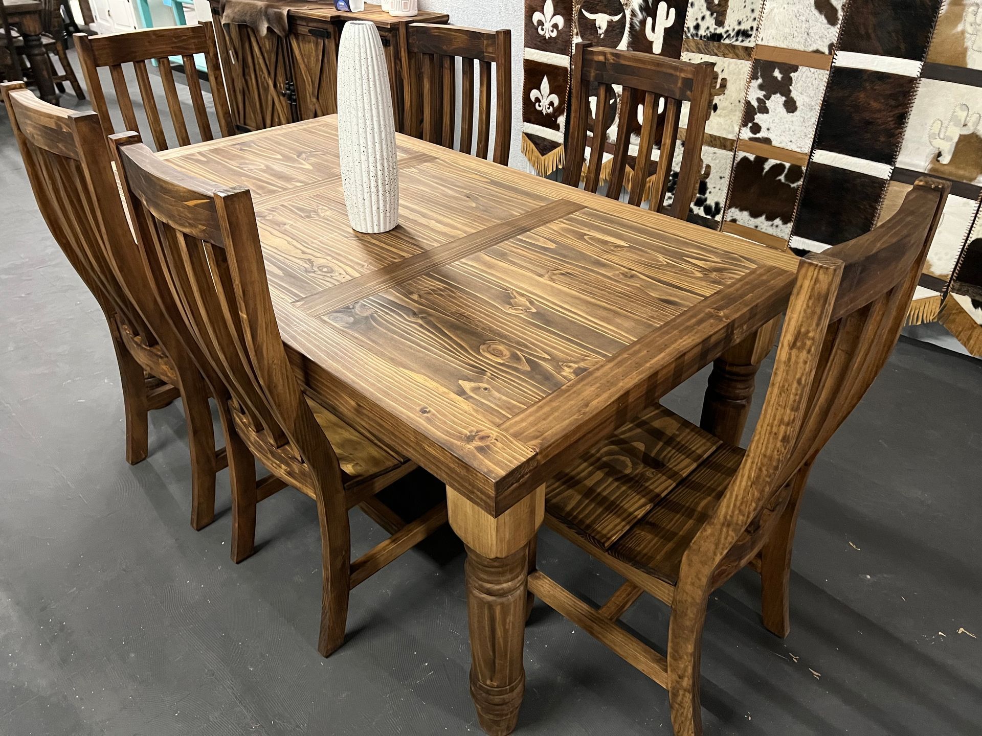 Wooden dining set in a well-lit room with a buffet and stairs in the background.