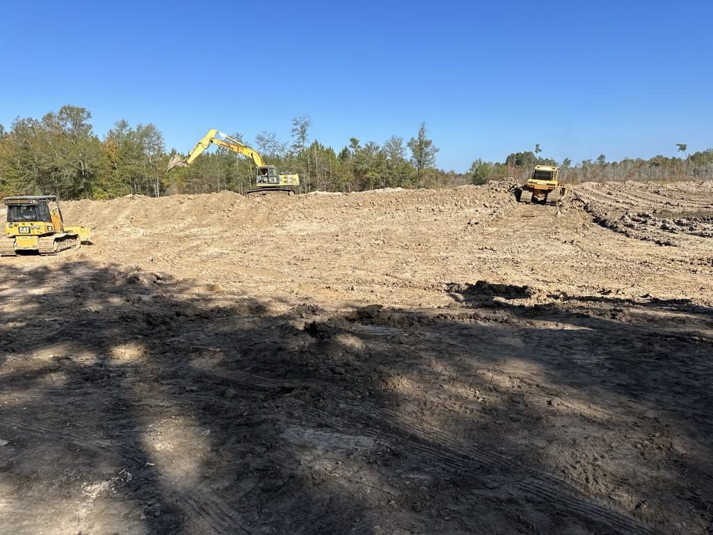 A group of construction vehicles are working on a dirt field.